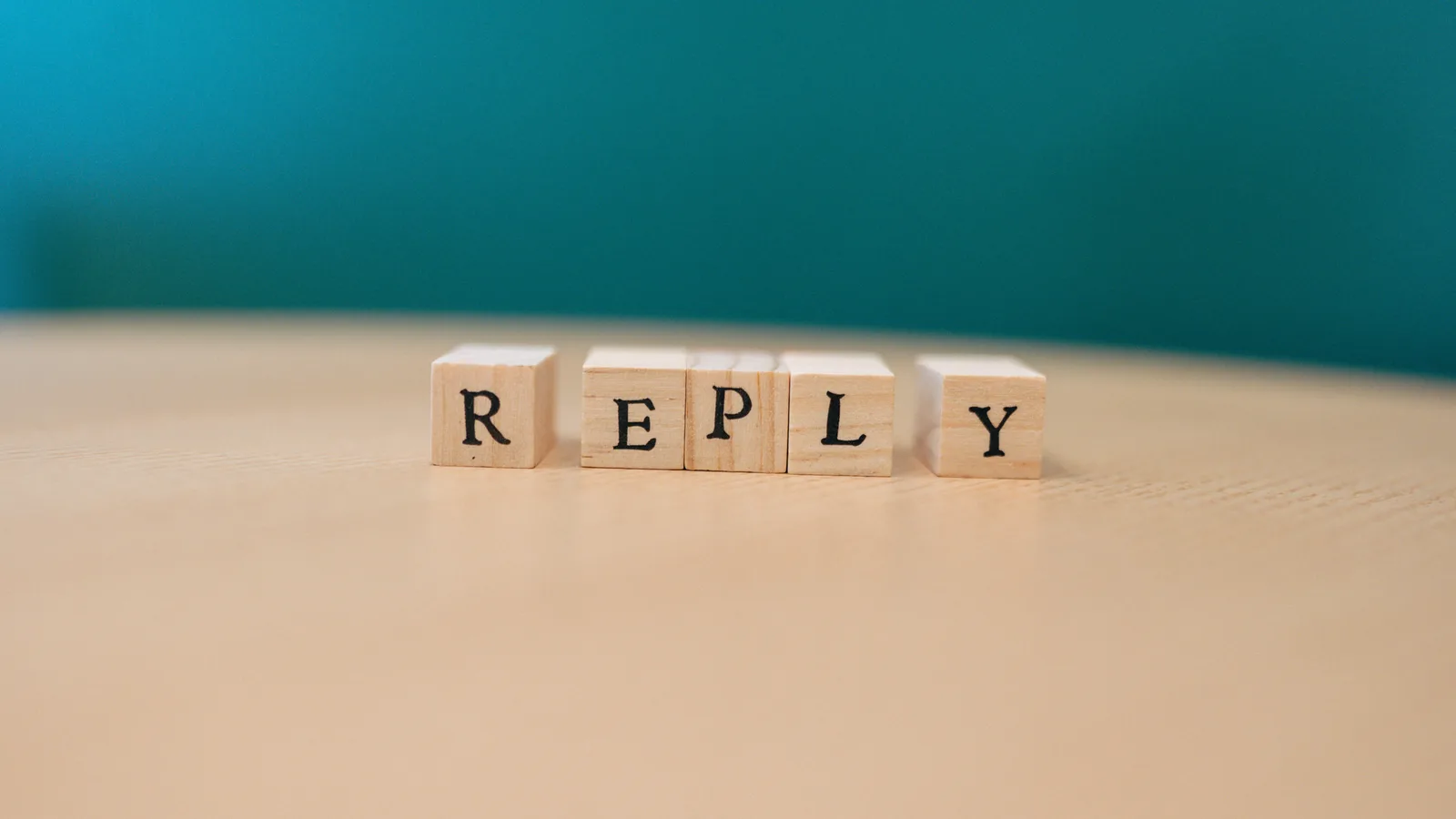 Close-up of wooden blocks spelling 'REPLY' over a wooden surface.