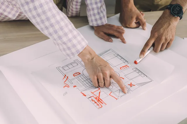 Hands pointing and discussing a floor plan in a collaborative workspace setting. Kundenkritik für Verbesserungen nutzen