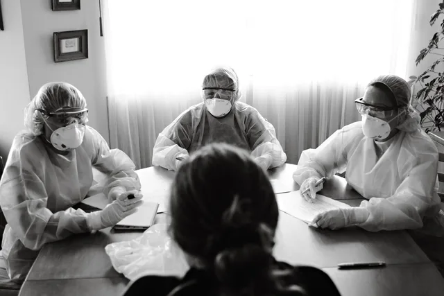 Black and white photo of healthcare team in PPE holding a meeting indoors. Reputationsvorfälle vorbereiten